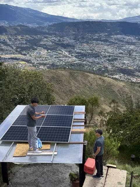Técnicos instalando módulos solares sobre una cubierta con vista a Quito.
